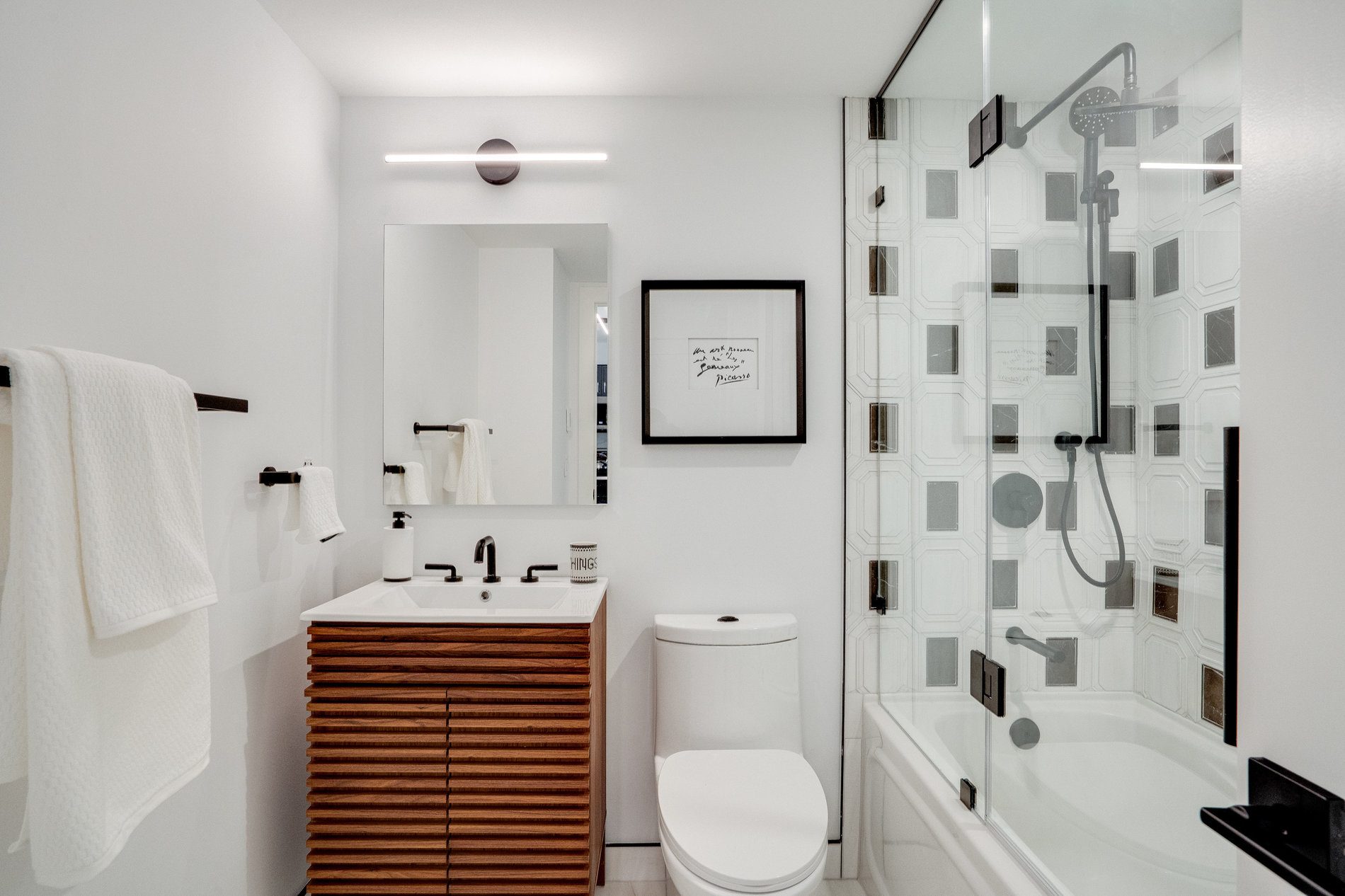 Walnut slatted vanity and a glass tub shield over patterned marble tile in an Etobicoke condo bathroom
