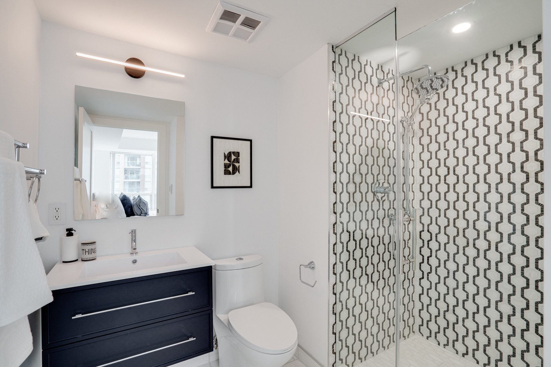 Walk-in glass shower with black and white geometric marble tile and a navy floating vanity, Etobicoke condo
