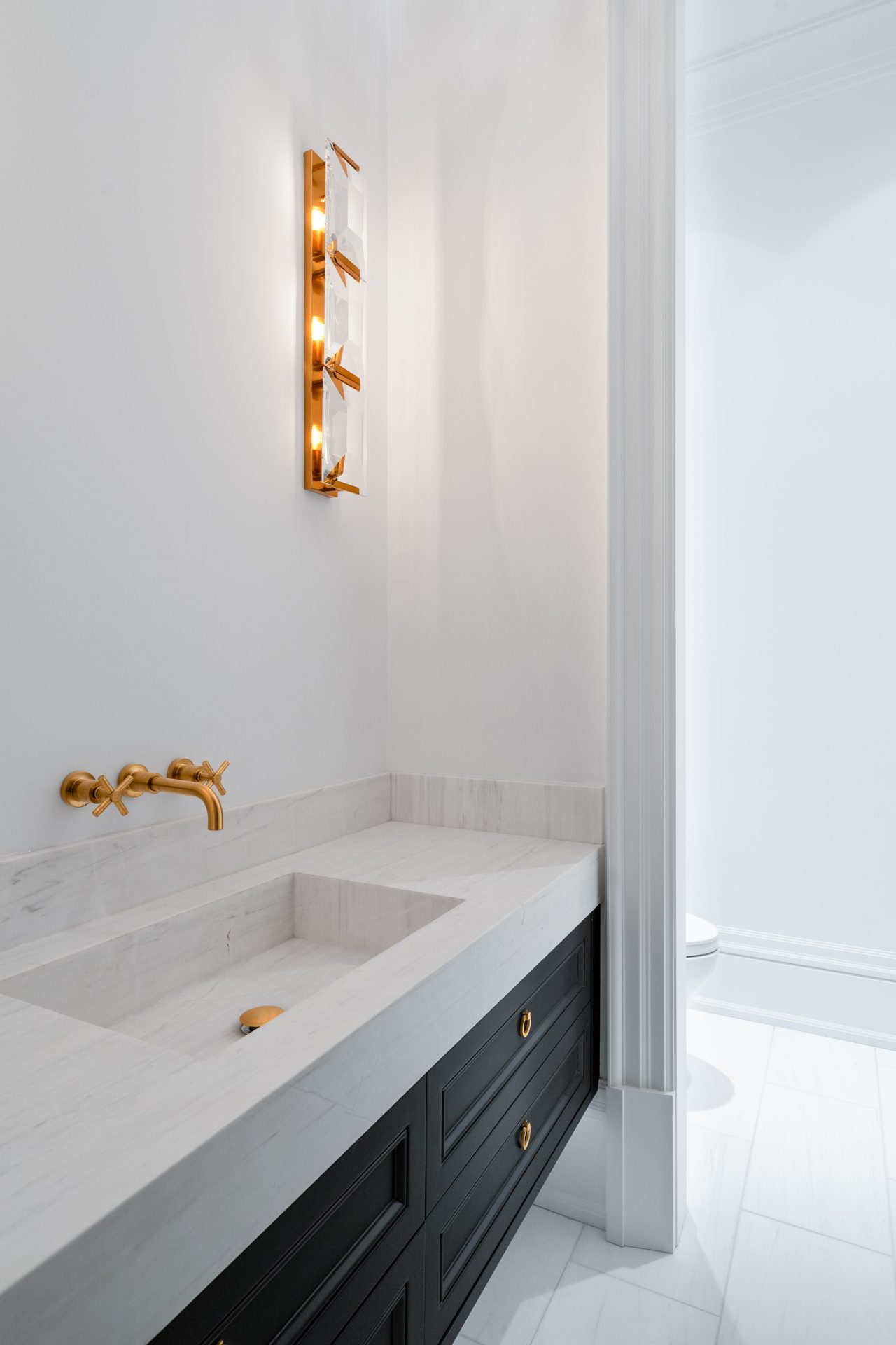 Marble vanity with an integrated sink, a brushed gold wall faucet and a crystal sconce, Thornhill