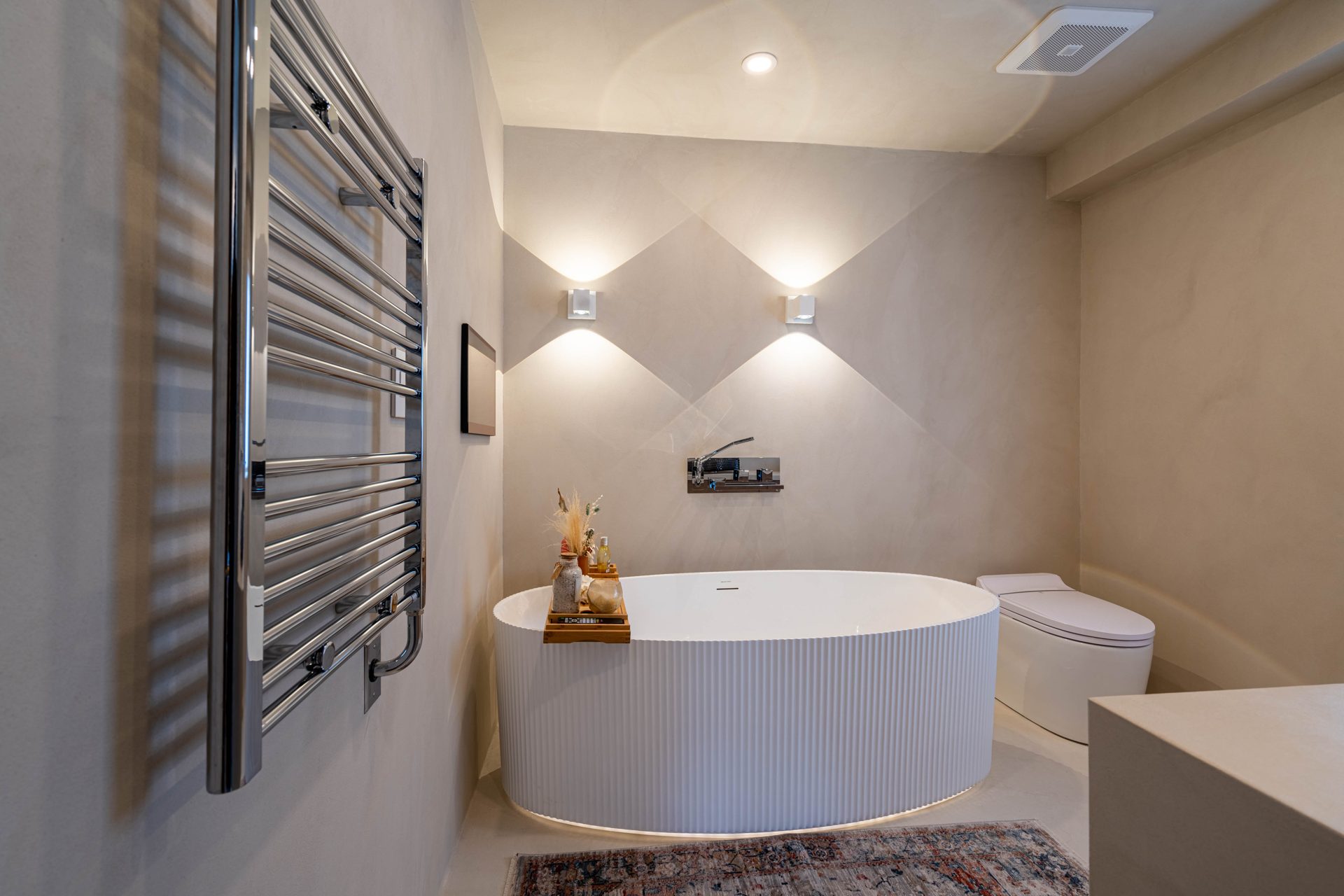 Fluted freestanding tub with a wall mounted filler, wall washer sconces and a heated towel rail in microcement, Richmond Hill