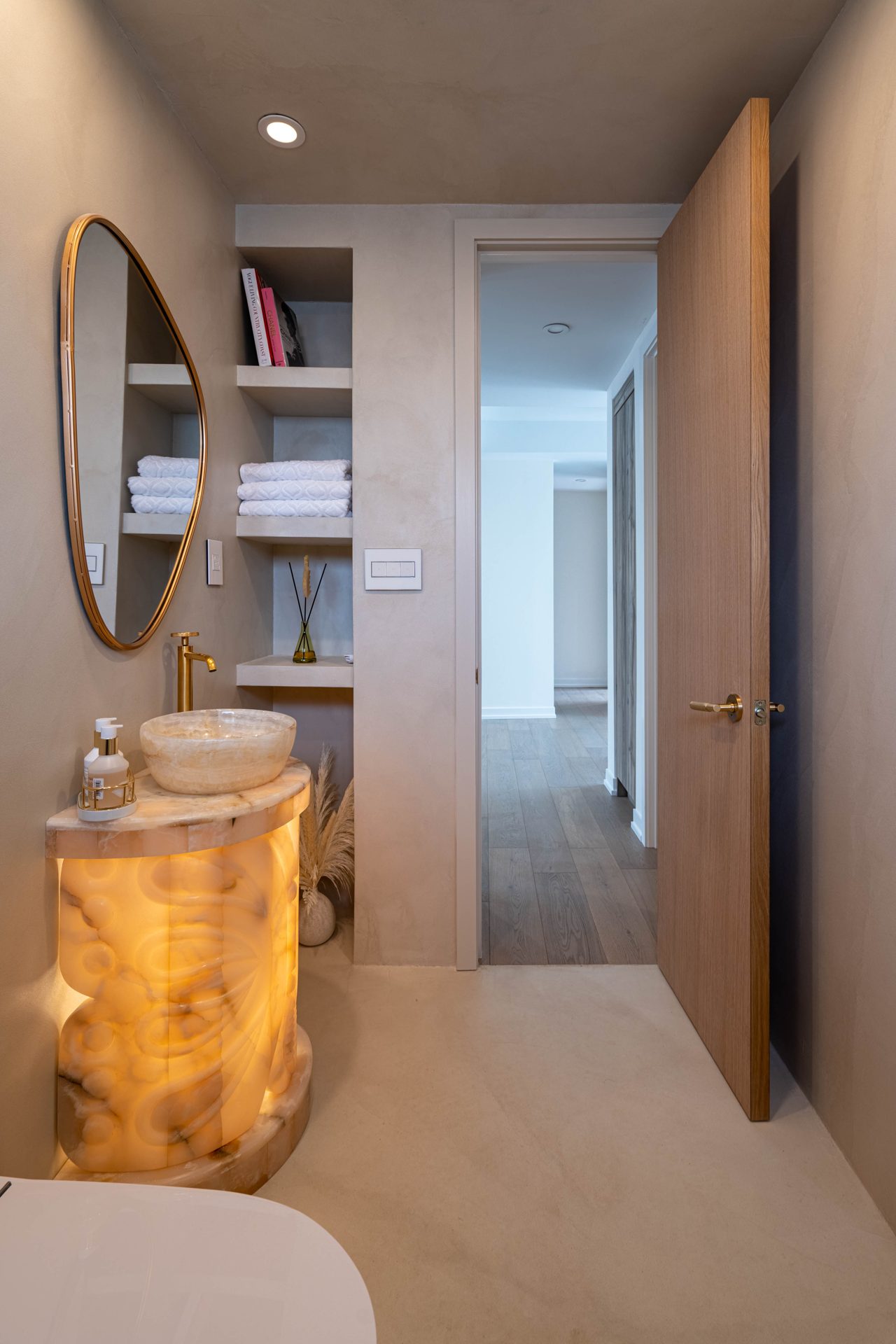 Backlit onyx pedestal vanity with a vessel sink and brass faucet in a plaster-finish powder room, Richmond Hill
